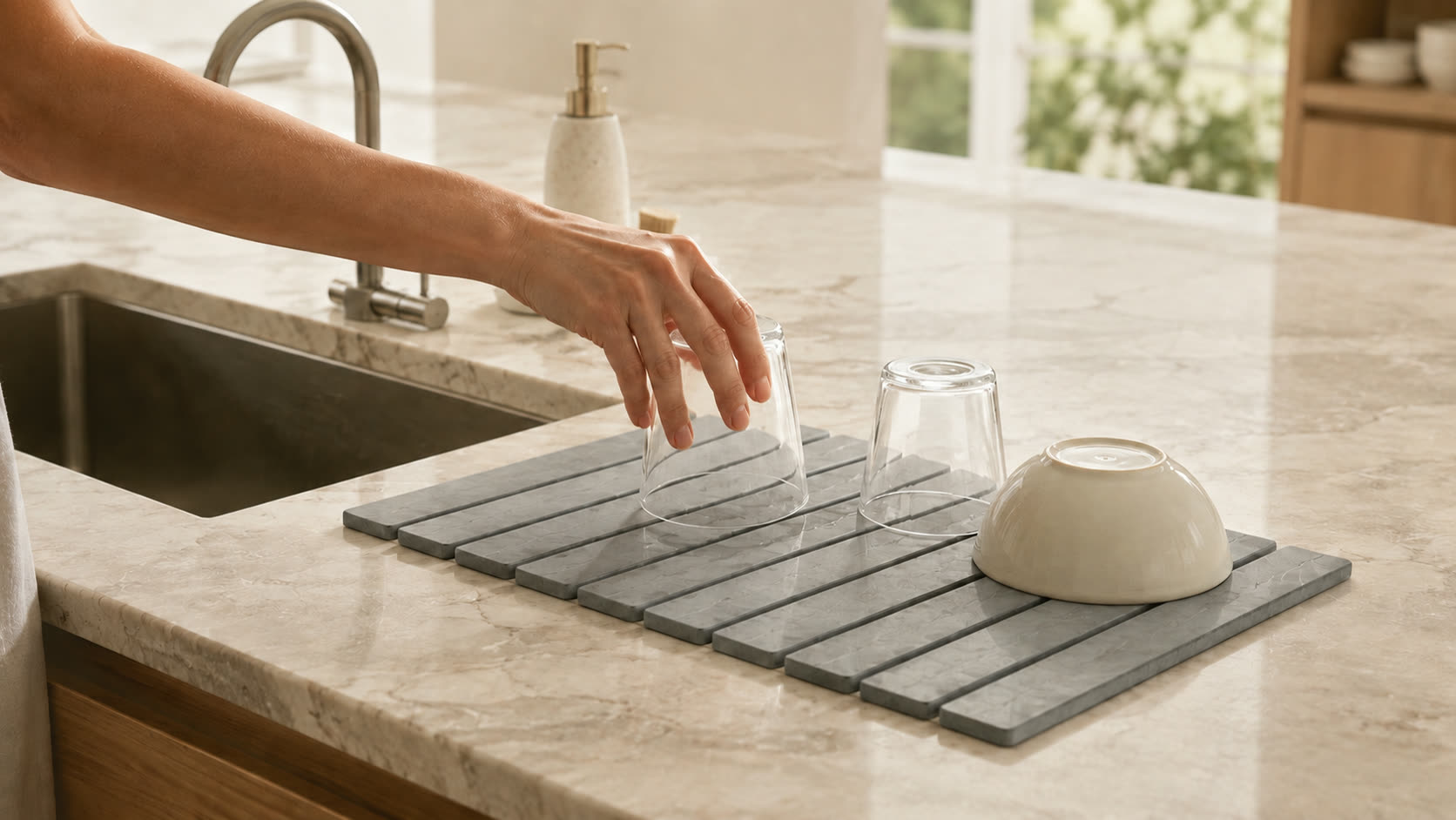 Hand placing a glass to dry on the Trivelle stone drying mat by a kitchen sink