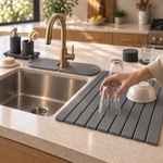 A hand setting an upturned glass on the Trivelle stone drying mat to air-dry beside the kitchen sink