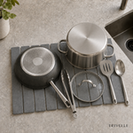 Overhead view of the stone drying mat holding a pan, pot, glass lid, tongs, and utensils by the sink