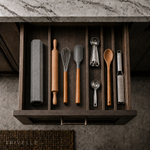 The folded stone drying mat stored upright in a wooden kitchen drawer beside a rolling pin, whisk, spatula, and measuring spoons