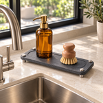 The stone sink caddy from the Essential Kitchen Set, raised on stainless steel legs beside the sink. Amber soap bottle and brush shown for styling, not included