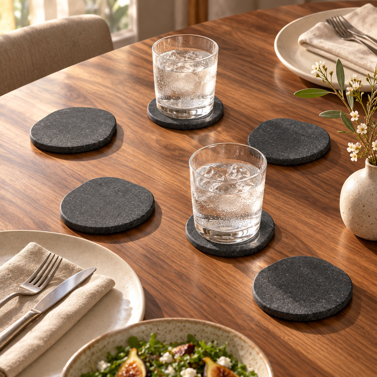 The six stone coasters from the Essential Kitchen Set on a dining table under glasses of iced water. Glasses and tableware shown for styling, not included